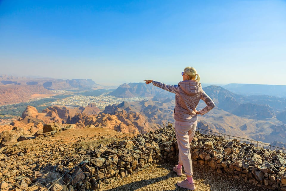 Turista rubia caminando en el desierto admirando el monumental Qasr Al Farid, un solitario Nabatae