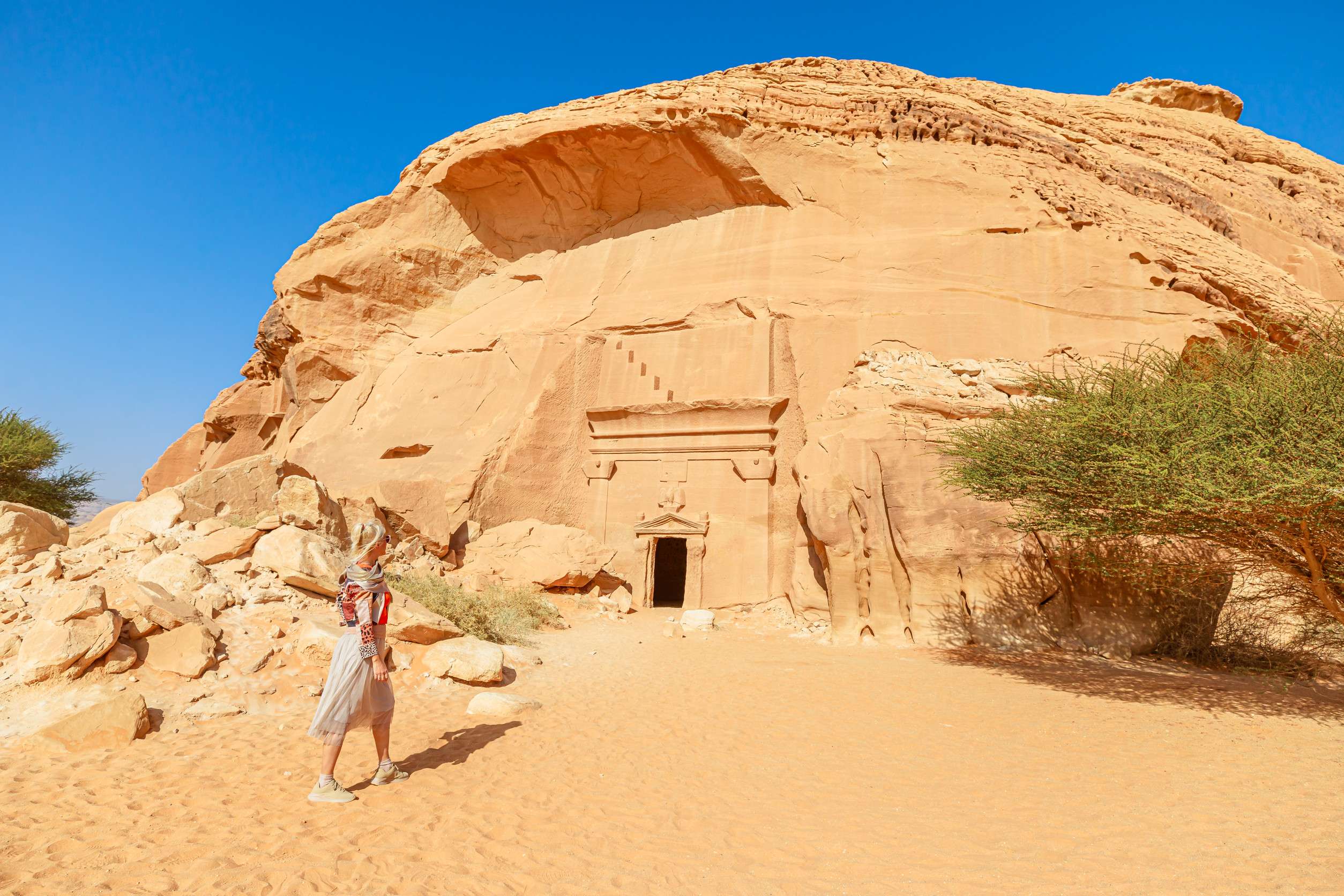Blonde Tourist Walking In The Desert Next To Of Jabal Albanat And Giant Rock Cut Tomb Of The
